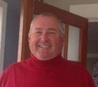 A man in red shirt smiling for the camera.